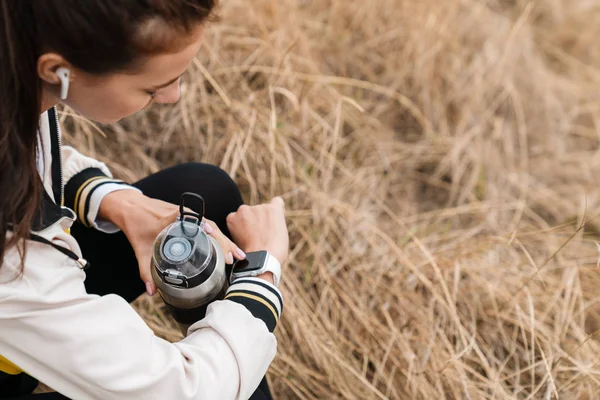 Обрезанное фото милой брюнетки с помощью умных часов и бутылочки — стоковое фото