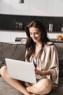 Kanepede dizüstü bilgisayar kullanan güzel bir kadın resmi. 