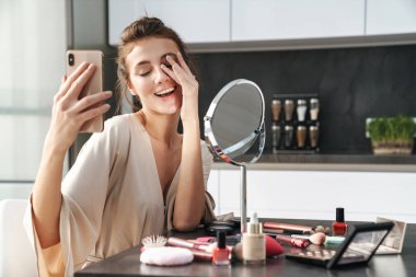 Yüzüne makyaj yaparken selfie çeken genç bir kadın görüntüsü