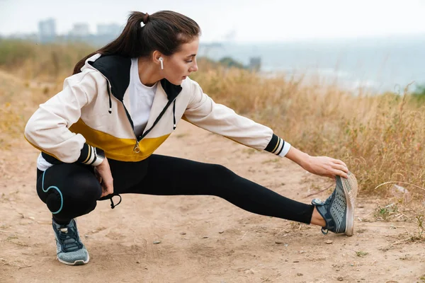 Photo of nice athletic woman using earpods and doing exercise — Stock Photo, Image