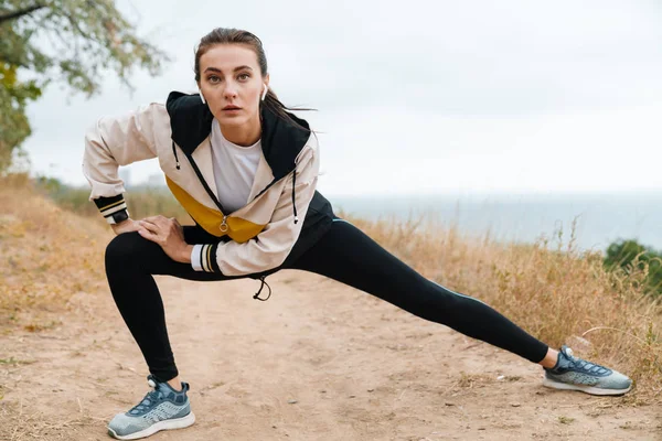 Foto de una mujer atlética agradable usando auriculares y haciendo ejercicio —  Fotos de Stock