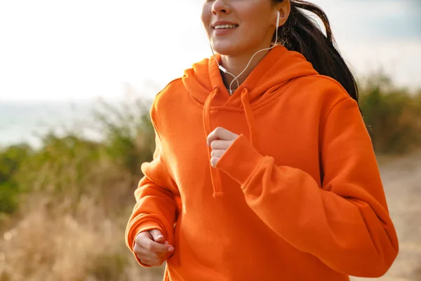 Foto de mujer atlética sonriente usando auriculares mientras corre — Foto de Stock