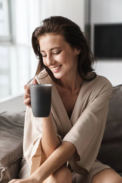 Image of young woman sitting on sofa at home and drinking tea in — 스톡 사진