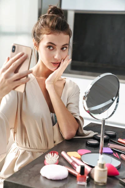 Imagen de una mujer joven tomando foto selfie mientras se aplica la cara mak —  Fotos de Stock