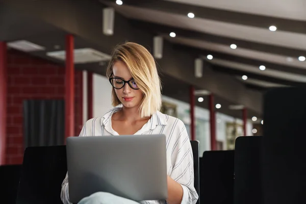 Photo of serious blonde woman working on laptop while sitting — Stock Photo, Image