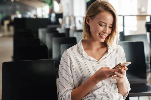 Photo d'une femme blonde heureuse tapant sur son smartphone en étant assise — Photo