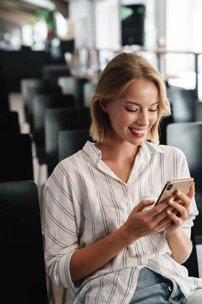 Fénykép vidám szőke nő gépelés okostelefon ülés közben — Stock Fotó