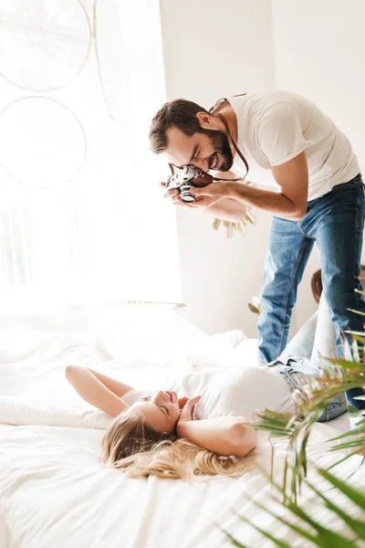 Wesoła młoda para robi zdjęcia w domu, leżąc na łóżku — Zdjęcie stockowe