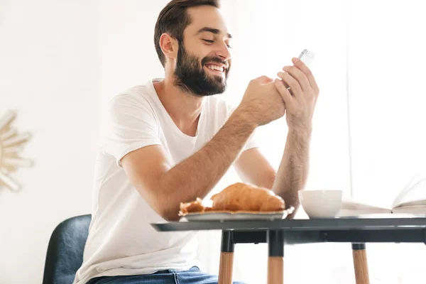 Smiling young man having breakfast at the kitchen — Stock Photo, Image