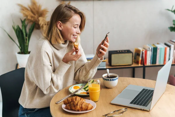 Fénykép boldog szőke nő használja a mobiltelefon reggeli közben — Stock Fotó