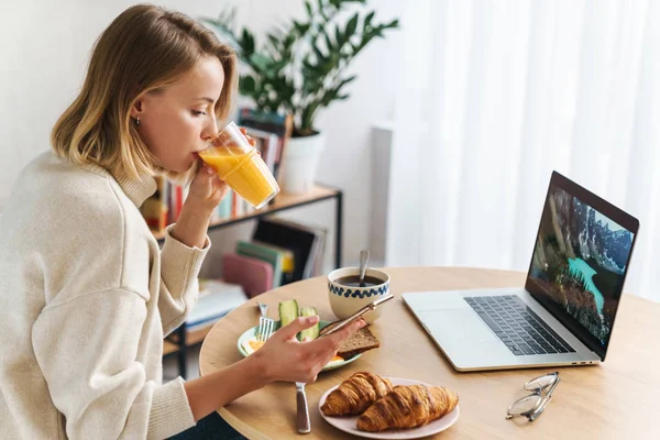 Foto einer lächelnden Frau mit Laptop und Handy beim Frühstück — Stockfoto