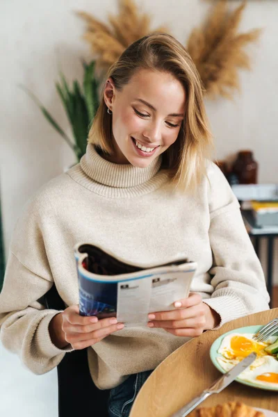 Fénykép vidám szőke nő olvasás magazin reggeli közben — Stock Fotó