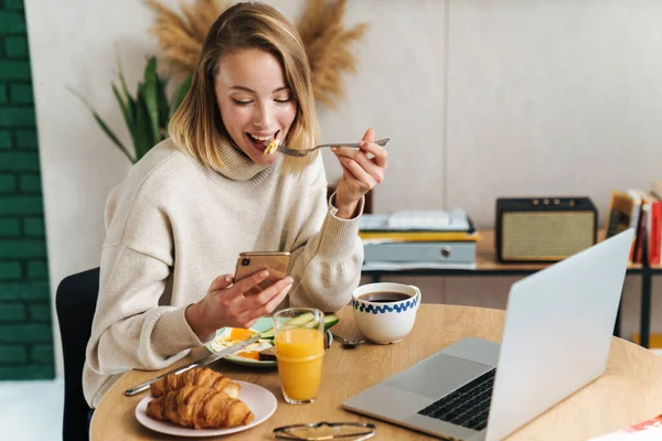 Fénykép mosolygós szőke nő használja a mobiltelefon reggeli közben — Stock Fotó