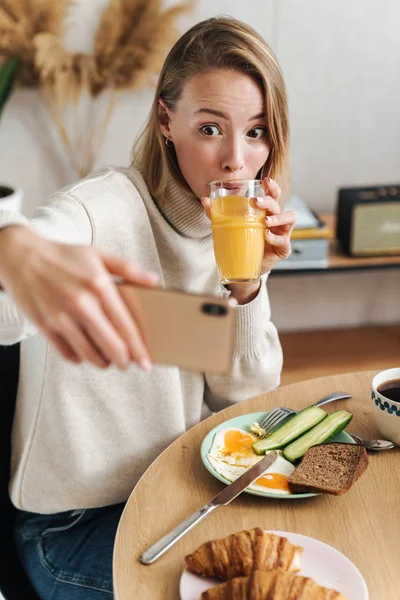 Фото забавной женщины, делающей селфи по мобильному телефону во время завтрака — стоковое фото