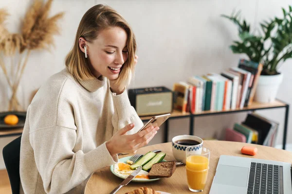 Foto einer Frau mit Handy und Ohrhörern beim Frühstück — Stockfoto