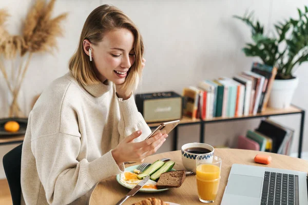 朝食をとりながら携帯電話やイヤホンを使っている女性の写真 — ストック写真