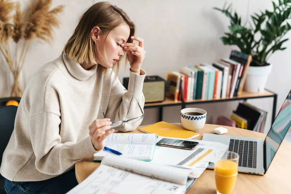 Photo d'une femme fatiguée prenant des notes dans un cahier d'exercices et utilisant un ordinateur portable — Photo