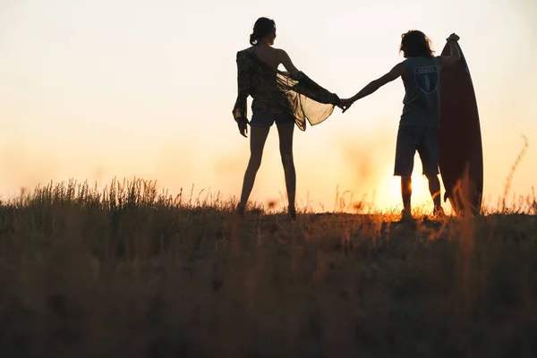 Silhueta de feliz jovem casal de mãos dadas enquanto olha para o pôr do sol — Fotografia de Stock