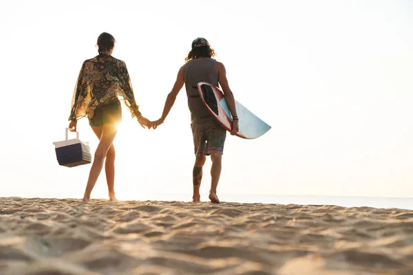 Foto vom Rücken des jungen Paares mit Surfbrett und Kühltasche — Stockfoto