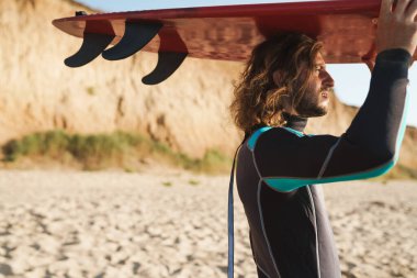 Yürürken elinde sörf tahtası olan odaklanmış sakallı adamın fotoğrafı.