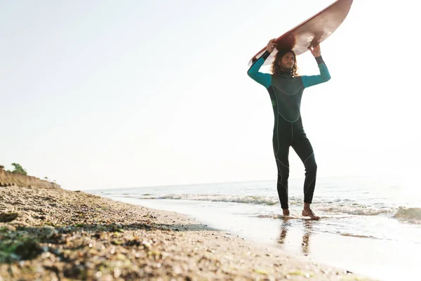Foto del atlético hombre masculino sosteniendo la tabla de surf mientras camina —  Fotos de Stock