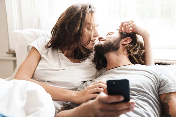 Aimer couple à l'intérieur à la maison se trouve en utilisant le téléphone mobile ensemble . — Photo
