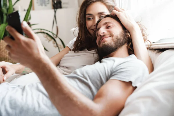 Pareja de amor en el interior de casa se encuentra utilizando el teléfono móvil juntos . — Foto de Stock