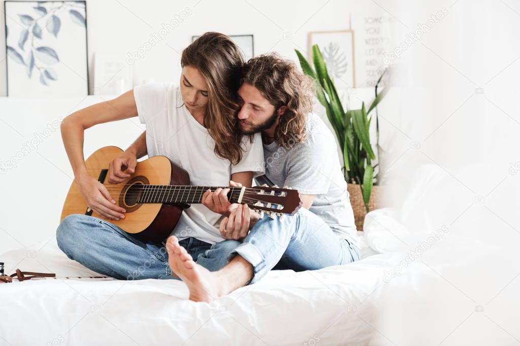 Loving couple indoors at home play on guitar.