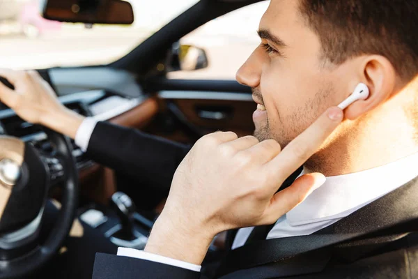 Foto de um jovem empresário sorrindo usando o fone de ouvido enquanto dirige o carro — Fotografia de Stock
