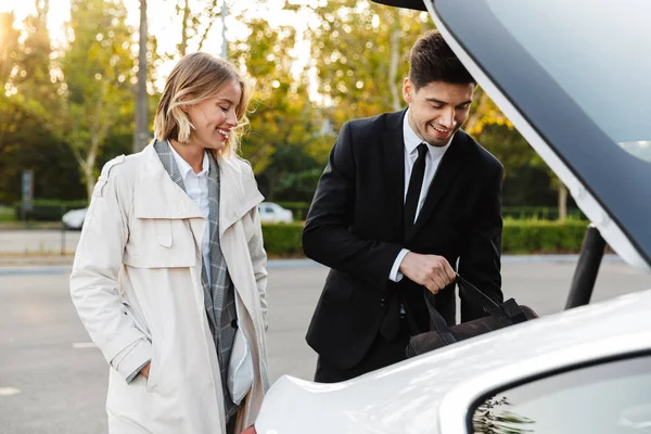 Photo of smiling colleagues man and woman putting bag in car trunk — Stok fotoğraf