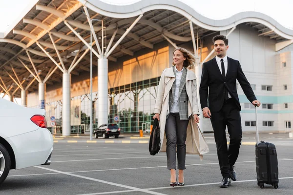 Photo of happy colleagues man and woman walking with suitcase