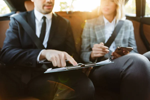 Image of businesslike man and woman sitting in car with working — Stockfoto
