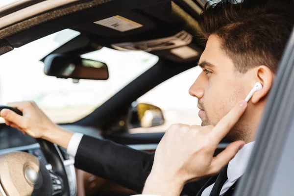 Foto de um jovem empresário sério usando o fone de ouvido enquanto dirige o carro — Fotografia de Stock