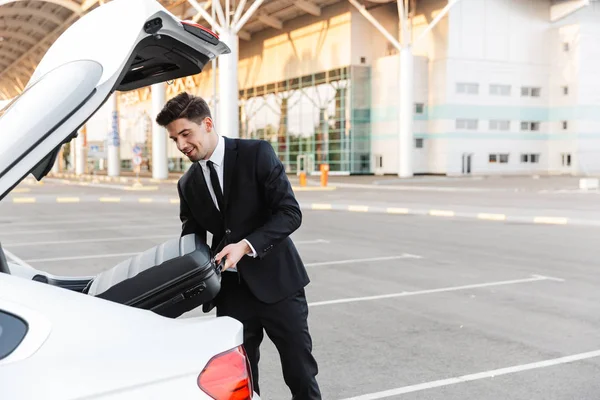 Photo d'un homme d'affaires souriant mettant une valise dans un coffre de voiture — Photo