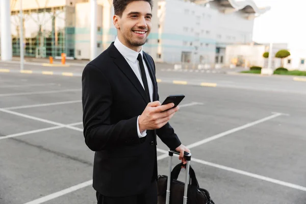 Image of businesslike man standing with luggage and cellphone ou — ストック写真