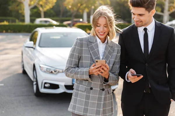 Photo of smiling man and woman using cellphones while walking — Stockfoto