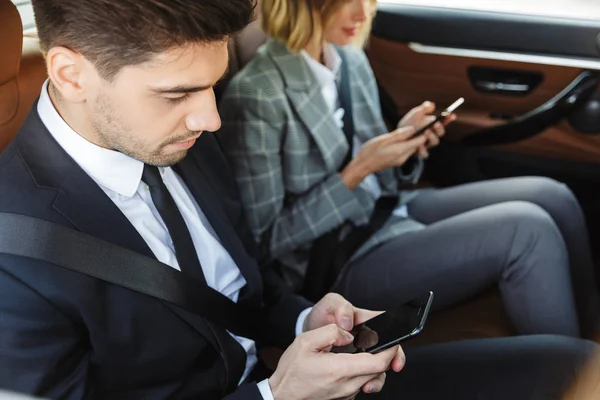 Photo of focused colleagues man and woman using cellphones while going in car — 图库照片