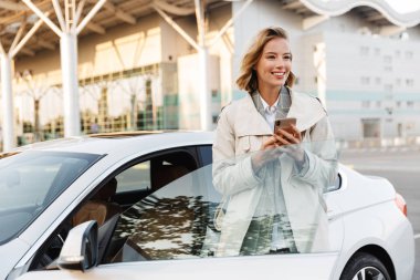 Image of businesslike woman standing by car and using cellphone 
