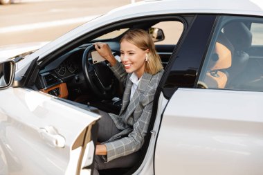 Photo of smiling businesswoman using earpod while getting out of car