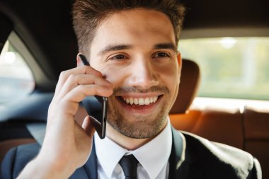 Image of young businesslike man in suit talking on cellphone in 