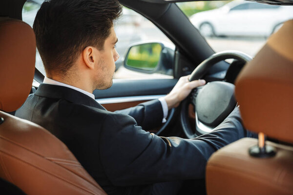 Фотография ориентированного молодого бизнесмена, который смотрит вперед во время вождения автомобиля

