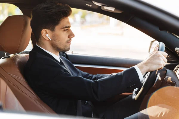 Foto do jovem empresário focado usando o fone de ouvido enquanto dirige o carro — Fotografia de Stock
