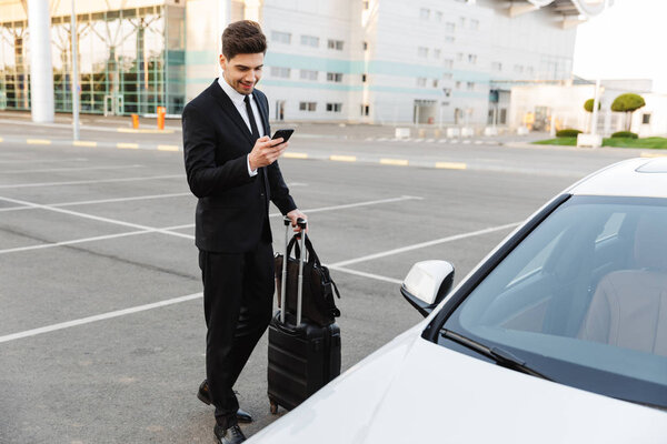 Image of young caucasian businesslike man standing with travel l