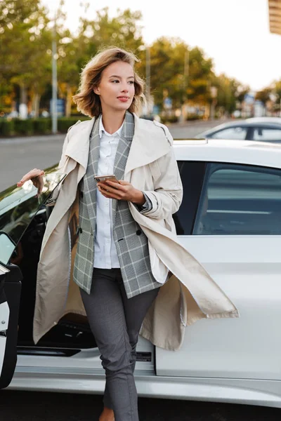 Фото молодой предпринимательницы, поющей сотовый телефон, выходящей из машины — стоковое фото