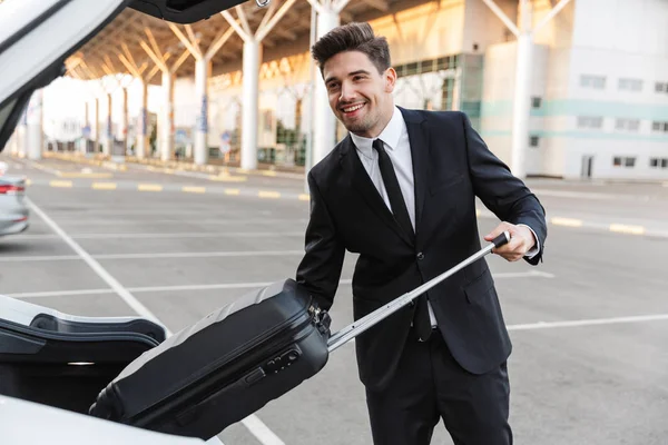 Photo of happy businessman putting suitcase in car trunk — 스톡 사진