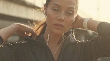 Kulaklıklı, kapüşonlu ve dışarı bakan Asyalı güzel bir spor kadının yakın görüntüsü.