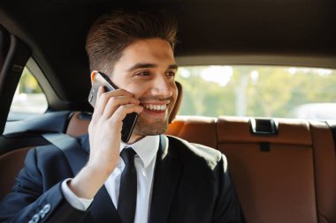Image of young businesslike man in suit talking on cellphone in 