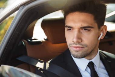 Image of young caucasian businesslike man in suit riding in car
