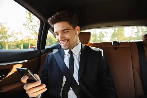 Image of young businesslike man using earbuds and cellphone in c — 图库照片