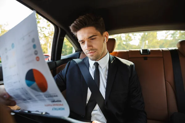 Image of young businesslike man riding in car with working docum — Stockfoto